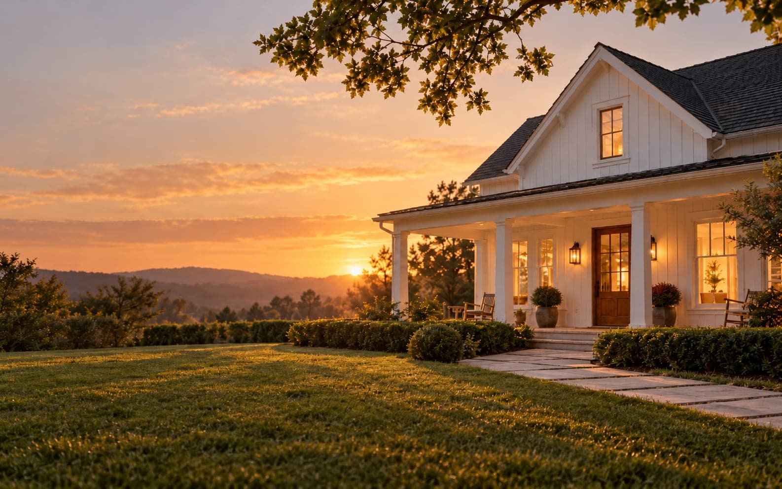A white farmhouse with a lit front porch at sunset
